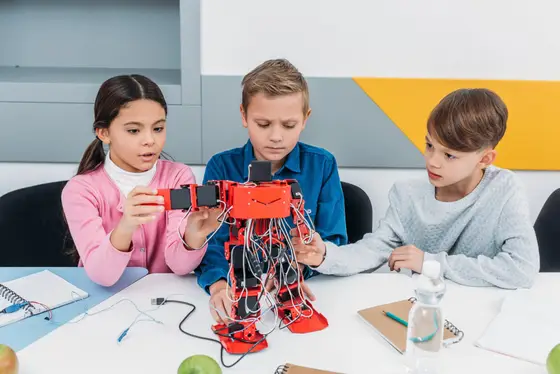 Trois enfants de 9 à 12 ans montent un robot humanoïde rouge lors d’un atelier de robotique