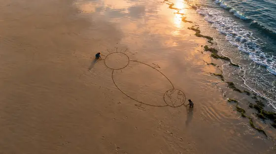 Technique Feynman : deux enfants dessinent le Soleil et la Terre dans le sable mouillé d’une plage au lever du jour